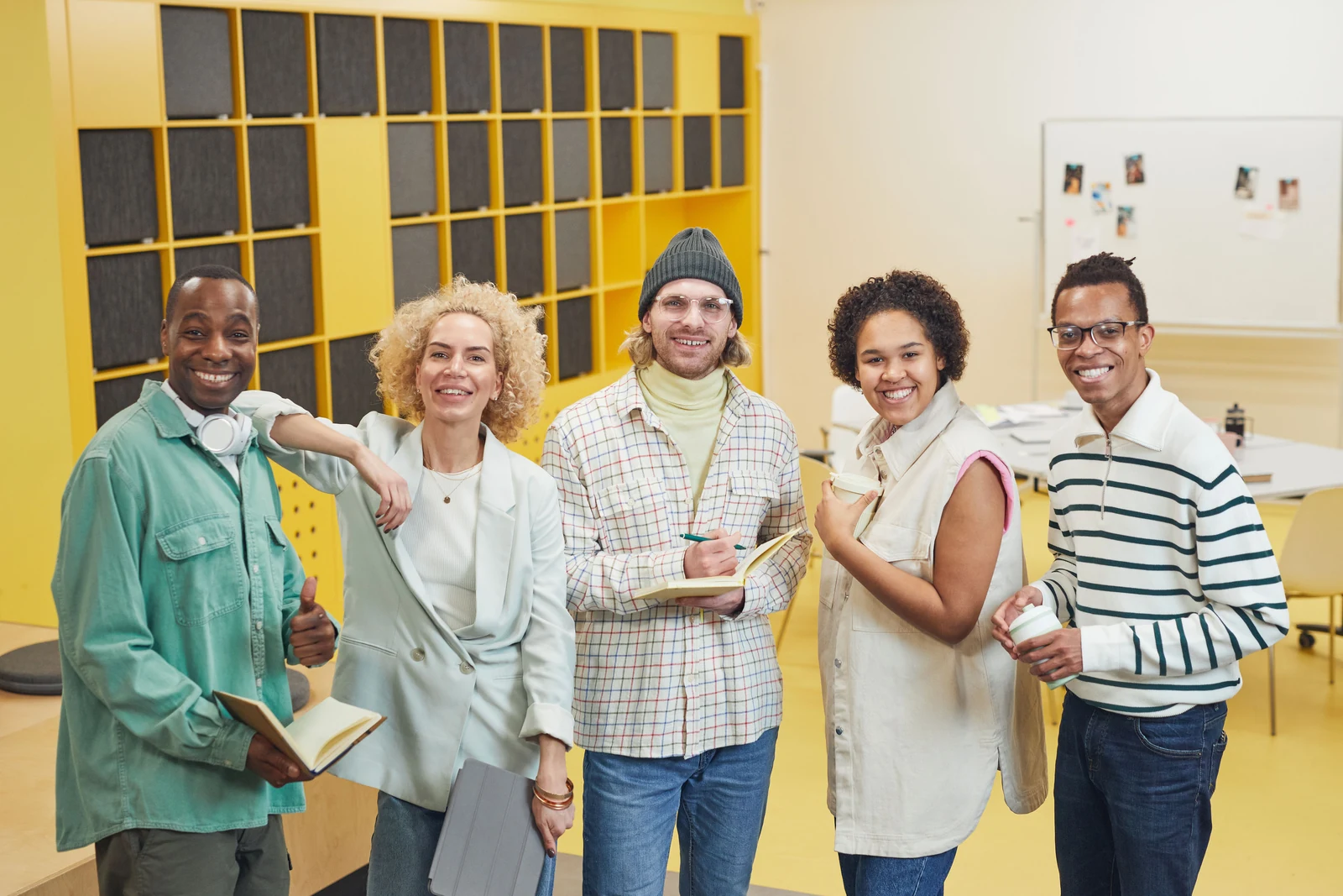 A diverse group of five smiling colleagues in casual clothes standing together in a bright, colorful office